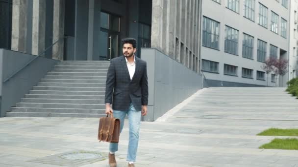 Pohledný muslimský obchodník ve stylovém společenském oblečení, kráčející venku s hnědým koženým kufříkem v rukou. Vousatý mladík na cestě do práce. Muslimský podnikatel s kufrem chůze venku. — Stock video