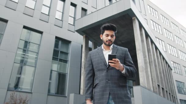 CloseUp of Attractive Young Businessman pomocí Smartphone a úsměvy. Píšu zprávy, když stojím poblíž moderní kancelářské budovy. Nosí klasický oblek. Sociální síť. Aplikace. Smartphone. Arabský muž — Stock video