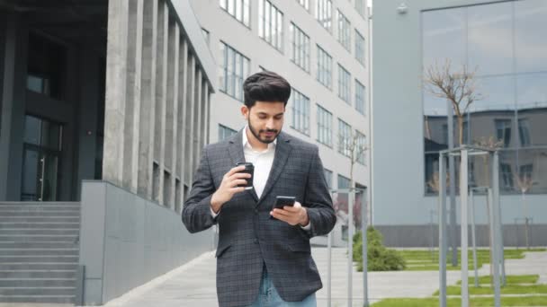Arabský muž v obleku stojí poblíž kancelářské budovy s moderním smartphonem a šálkem kávy v ruce. Koncept lidí, moderní životní styl. Arabský muž pomocí smartphonu a pití kávy — Stock video