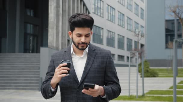 Arabian man i kostym står nära kontorsbyggnad med modern smartphone och kopp kaffe i händerna. Begreppet människor, modern livsstil. Bushy skäggig man skriva meddelanden på mobiltelefon. — Stockvideo