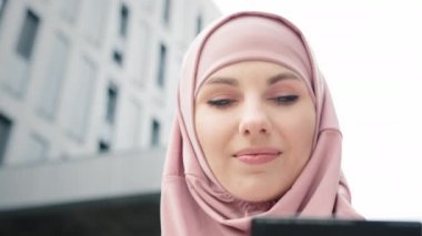 Tesettürlü çekici bir kadın ve modern akıllı telefon ve kredi kartını elinde tutan resmi kıyafetler. Müslüman kadın kredi kartı ve cep telefonuyla alışveriş yapıyor. İnsan kavramı, teknoloji ve alışveriş