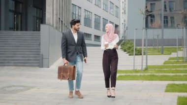 İki müslüman ofis çalışanı dışarıda gülerek ve sohbet ederek yürüyorlar. Takım elbiseli yakışıklı bir adam bavul ve akıllı telefon taşıyor, tesettürlü çekici bir kadın elinde kahve ve dosya tutuyor..