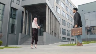 Müslüman iş ortaklarının resmi giysiler içinde sokakta el sıkışırken yan görünüşü. Anlaşma kavramı. İş ortakları el sıkışıyor. İş adamları Müslüman bir kadını selamlıyor. Modern Ofisin yakınında.