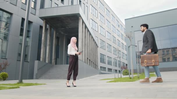 Vista lateral de los socios musulmanes en ropa formal de pie en la calle y estrechando las manos. Concepto del trato. Socios de negocios estrechando las manos. Joven empresario saluda a una mujer musulmana. — Vídeos de Stock