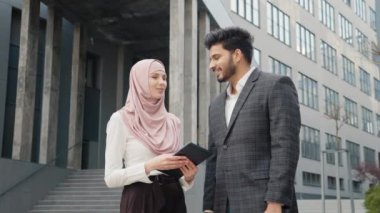 Gülümseyen Arap iş arkadaşları şehrin caddesinde durup modern akıllı telefondan selfie çekiyorlar. Elinde dijital tablet olan tesettürlü çekici bir kadın cep telefonu olan yakışıklı bir adam. Gülümseyen iş