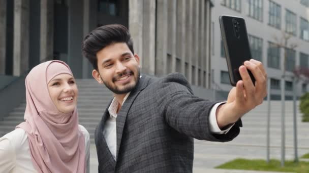 Glimlachende Arabische collega 's die op straat staan en selfie nemen op een moderne smartphone. Een vrouw in hijab met een digitale tablet in de buurt van haar moslimcollega. Begrip "bedrijf" — Stockvideo