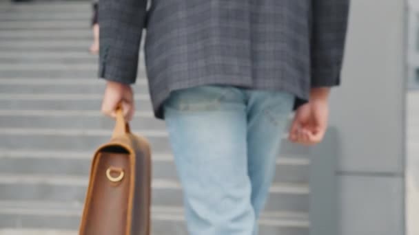 Feche-se o homem com a mala a subir as escadas. Homem muçulmano em desgaste formal subindo escadas enquanto mulher em hijab sentado perto e trabalhando no laptop. Dois colegas fazendo trabalho remoto ao ar livre. — Vídeo de Stock