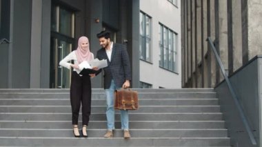İş kıyafetleri içinde başarılı çok kültürlü iş arkadaşları iş amaçlarına ulaşıyor. Mutlu Arap iş kadını havaya kağıt kustu. Arka planda iş merkezi.