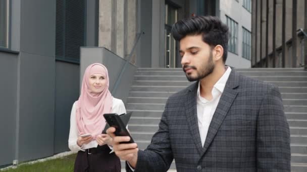 Mujer hombre de negocios en hijab y musulmán hombre de negocios estrechando la mano el uno al otro, mientras que de pie al aire libre cerca del moderno centro de oficinas. Concepto de cooperación y éxito. Compañeros musulmanes caminando al aire libre — Vídeos de Stock