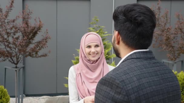 Zakenvrouw in hijab en moslim zakenman schudden elkaar de hand terwijl ze buiten in de buurt van modern kantoorcentrum staan. Concept van samenwerking en succes. Zakelijke partners schudden handen — Stockvideo