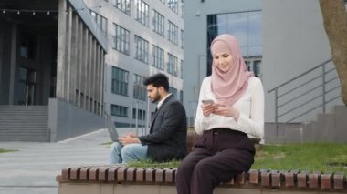 Laptopta çalışan Müslüman adamın yanındaki bankta otururken cep telefonu kullanan tesettürlü çekici kadın. Uzaktan kumandalı iş için modern aletler kullanan iki serbest çalışan. Hindu adam dizüstü bilgisayarla çalışıyor.