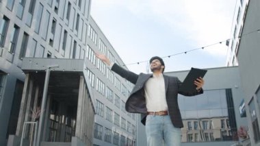 Mutlu Hindu işadamı dokümanları fırlatıyor. Modern ofis binasının yanında uzanan ve mutluluğu hisseden yakışıklı Hindu işadamının düşük açılı görüntüsü. İnsan duyguları kavramı
