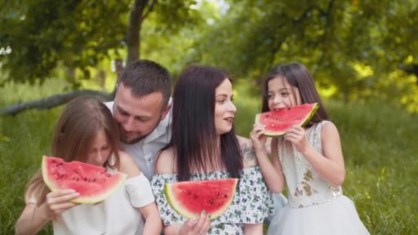 一个快乐的高加索家庭，有两个小女儿在户外吃西瓜。带着孩子的年轻父母一起度过了野餐的闲暇时间。孩子们在户外吃西瓜的快乐家庭 — 图库视频影像
