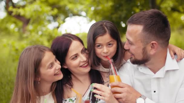 Padre sonriente, madre y dos hijas lindas que beben jugo fresco en el jardín verde mientras hacen un picnic de verano. Concepto de familia, ocio y relajación. Familia de picnic. Concepto de disfrute. — Vídeo de stock
