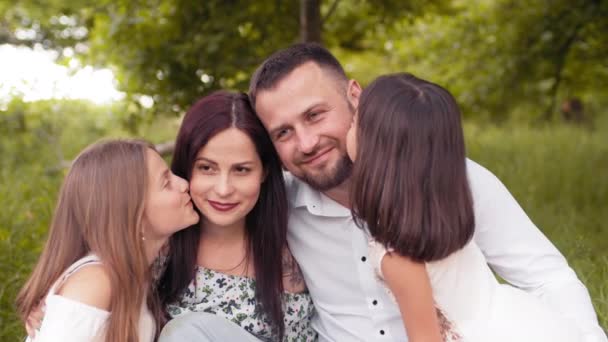 Dos hermanas guapas besando a su padre y a su madre durante el picnic de verano en el jardín verde. Hermosa familia caucásica relajándose juntos al aire libre. Concepto de amor y felicidad. Niñas besando padres — Vídeo de stock