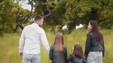 Çekici hamile anne ve babamın yeşil bahçede yürüyen iki küçük kızıyla el ele tutuşması. Genç bir kadın yaz günlerini çocuklarla temiz hava alarak geçiriyor. İki kızı olan ebeveynler.