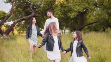 İki çocuklu pozitif aile yaz günlerini yeşil bahçede geçiriyor. Genç ebeveynler yürür ve arkada konuşurlar. Dört kişilik mutlu bir aile temiz havanın tadını çıkarıyor. İki çocuklu aile