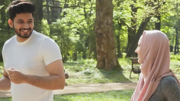 緑の公園で朝のランニングを楽しむアクティブな服の健康的なスポーツカップル。ヒジャーブ州のイスラム教徒の男性と女性は、新鮮な空気の訓練のために余暇を過ごしています。緑の公園で一緒に走るイスラム教徒の家族 — ストック動画
