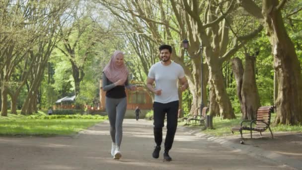 Muzułmanin i kobieta uciekają. Szczęśliwa para arabów uprawiająca jogging w parku. Zdrowa arabska para ciesząca się porannym bieganiem po zielonym parku. Pozytywna muzułmańska rodzina biegająca razem w zielonym parku. — Wideo stockowe