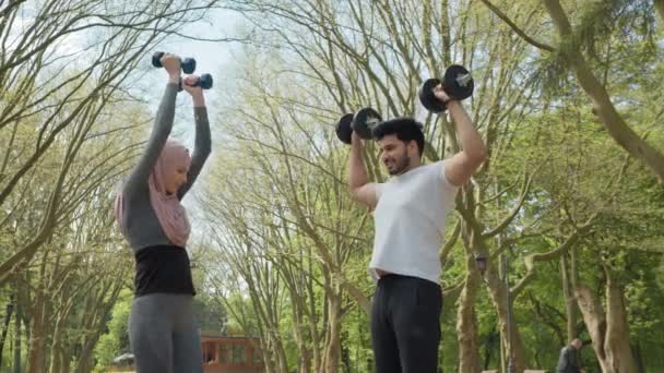 在夏季公园的晨练中，让健康的阿拉伯夫妇穿着运动服，用沉重的哑铃。人的概念，团结和训练。阿拉伯夫妇在锻炼时使用哑铃 — 图库视频影像