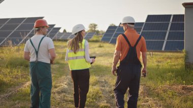 Büyük enerji santralinde çalışan işçiler güneş panelleriyle konuşuyor. Endüstriyel meslektaşlardan oluşan bir ekip. Güneş parkı. Alternatif enerji kavramı. Ekolojik yapı. Güneş panelleri alanı. Takım çalışması..