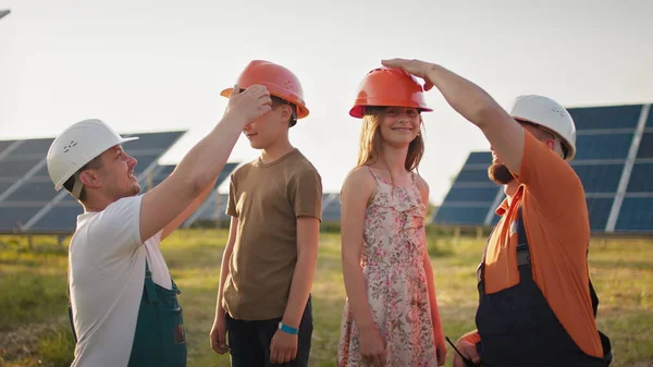 Barna kom på jobb for foreldrene sine. To fedre tok på seg hjelmer for barna sine og klemte dem på jobben. En ansatt i et solkraftverk med barn på jobb som smiler til kameraet. Far lykkelig – stockfoto