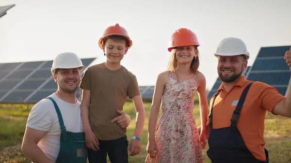 Lapset tulivat töihin vanhemmilleen. Kaksi isää laittaa kypärät lapsilleen ja halata töissä. Aurinkovoimalan työntekijä, jolla on työssä lapsia ja joka hymyilee kameralle. Isä onnellinen — kuvapankkivalokuva