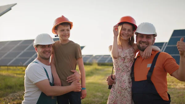 Lapset tulivat töihin vanhemmilleen. Kaksi isää laittaa kypärät lapsilleen ja halata töissä. Aurinkovoimalan työntekijä, jolla on työssä lapsia ja joka hymyilee kameralle. Isä onnellinen — kuvapankkivalokuva
