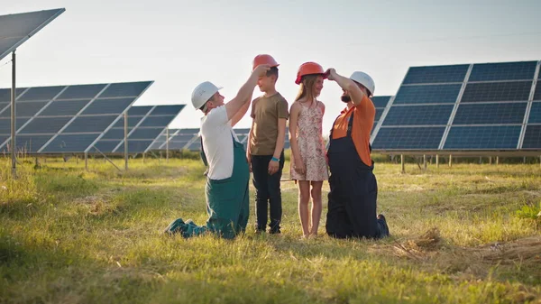 Kaksi aurinkovoimalan työntekijää toi lapsensa töihin ja laittoi suojakypärän lasten päähän. Lapset työskentelevät voimalaitosinsinöörien vanhempien kanssa. Isä ja lapsi — kuvapankkivalokuva