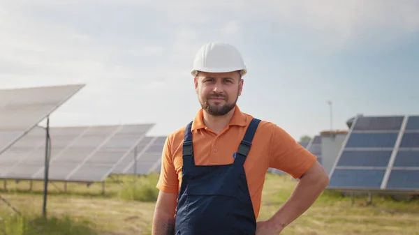 Portrett av en lykkelig mannlig ingeniør i beskyttelseshjelm foran kamera. Kjekk mann i uniform som smiler mens han står på solenergifarmen. Begrepet grønn energi. Industrifolk. Energi – stockfoto