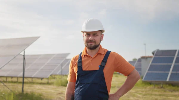 Portrett av en lykkelig mannlig ingeniør i beskyttelseshjelm foran kamera. Kjekk mann i uniform som smiler mens han står på solenergifarmen. Begrepet grønn energi. Industrifolk. Energi – stockfoto