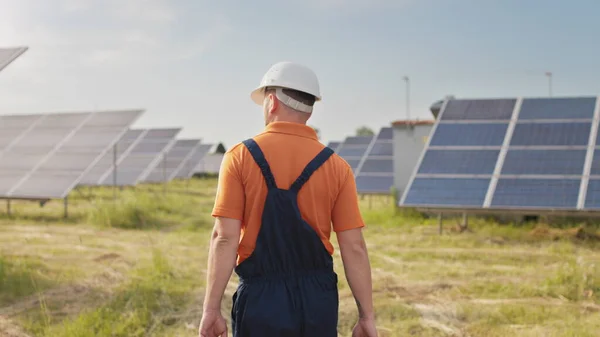 Teknisk vedlikeholdsarbeider i uniform kontrollerer solcellepanelenes virkemåte og effektivitet. Byggetekniker går mellom solcellepaneler på feltstasjon. – stockfoto