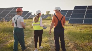 Büyük enerji santralinde çalışan işçiler güneş panelleriyle konuşuyor. Endüstriyel meslektaşlardan oluşan bir ekip. Güneş parkı. Alternatif enerji kavramı. Ekolojik yapı. Güneş panelleri alanı. Takım çalışması..
