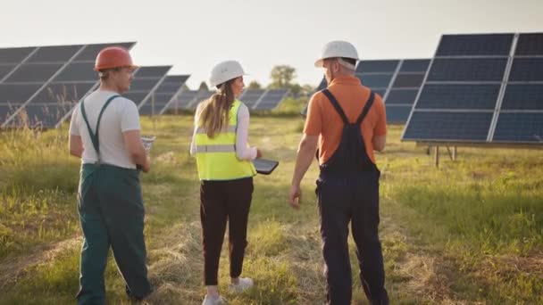 Workers talking on the big power station with solar panels.Team of industrial colleagues. Solar park. Alternative energy concept. Ecological construction. Solar panels field. Teamwork. — Stock Video
