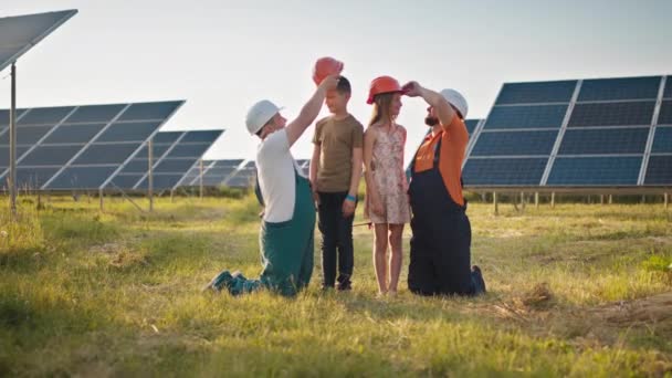 Due dipendenti della centrale solare hanno portato i loro figli al lavoro e messo un casco protettivo sulle teste dei bambini. Bambini al lavoro con i genitori degli ingegneri delle centrali elettriche. Padre e figlio — Video Stock