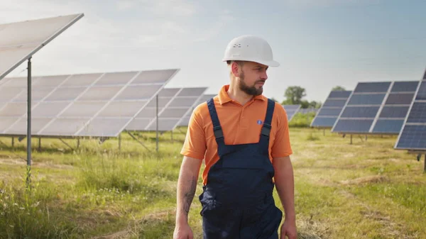 Teollisuusmies insinööri univormussa kävelemässä aurinkopaneelikentän läpi tutkittavaksi. Ekologinen rakenne. Aurinkovoimala, vihreän energian konsepti. Aurinkovoimaloiden kehittäminen ja energia — kuvapankkivalokuva