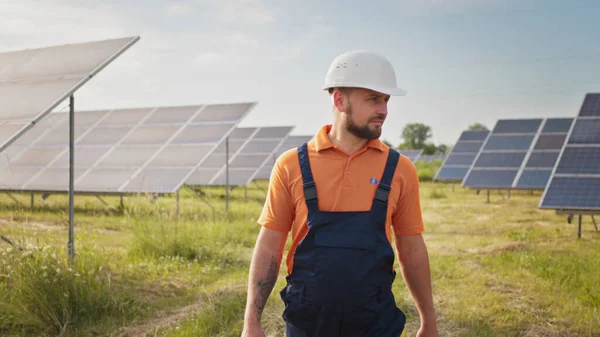 Industrial man engineer in uniform walking through solar panel field for examination. Ecological construction. Solar power station, Green energy concept. Solar station development and energy