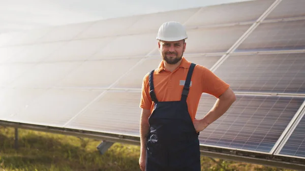 Lähikuva muotokuva mies sähkötyöntekijä suojakypärä seisoo lähellä aurinkopaneeli. Puhtaan energian tuotanto. Vihreä energia. Aurinkotila. Iloinen mies hymyilee seistessään aurinkoenergiatilalla — kuvapankkivalokuva