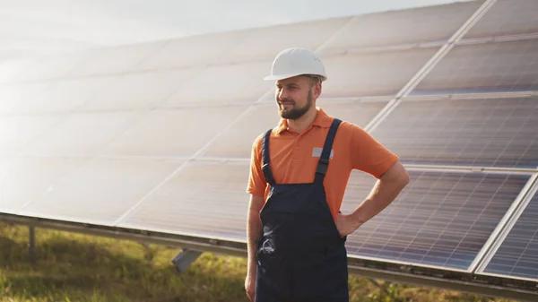 Lukk portrettet av en mannlig elektroarbeider i en beskyttelseshjelm som står ved solcellepanelet. Produksjon av ren energi. Grønn energi. Solpark. Munter mann smilende mens han står på solenergifarmen – stockfoto