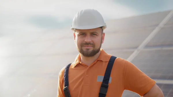Portrait of ecological expert industrial worker in uniform standing by solar panels installation. Construction of solar station. Workman. Clean energy production. Green energy. Ecological solar farm.