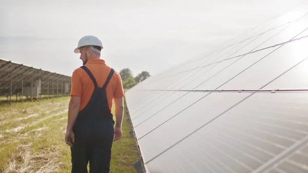 Virkapukuinen tekninen työntekijä tarkistaa aurinkosähköpaneelien toiminnan ja tehokkuuden. Käsitys sähköstä, ekologiasta. Aurinkopaneelien tila. Vihreä energia — kuvapankkivalokuva