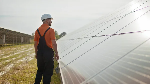 Ammattimainen miespuolinen insinööri suojakypärässä kävelee ekologisen aurinkovoimalan rakentamisessa. Käsite sähkö, ekologia, teknologiat. Aurinkopaneelien tila. Puhtaan energian tuotanto. Vihreä energia — kuvapankkivalokuva