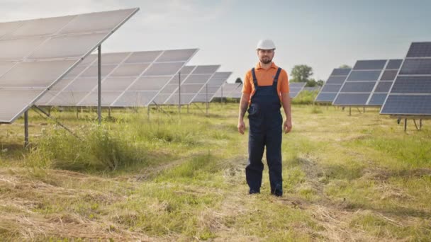 Professional man technician in hard hat walks on new ecological solar construction outdoors. Farm of solar panels. Concept of electricity, ecology, technologies. Portrait of engineer looking to camera — Stock Video