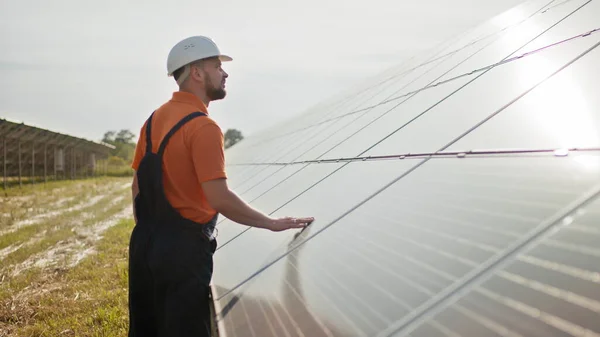 Ammattimainen miespuolinen insinööri suojakypärässä kävelee ekologisen aurinkovoimalan rakentamisessa. Käsite sähkö, ekologia, teknologiat. Aurinkopaneelien tila. Puhtaan energian tuotanto. Vihreä energia — kuvapankkivalokuva