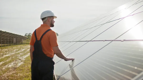 Ammattimainen miespuolinen insinööri suojakypärässä kävelee ekologisen aurinkovoimalan rakentamisessa. Käsite sähkö, ekologia, teknologiat. Aurinkopaneelien tila. Puhtaan energian tuotanto. Vihreä energia — kuvapankkivalokuva