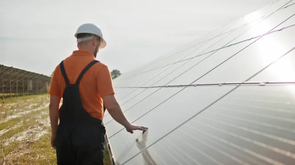 保護ヘルメットのプロの男性エンジニアは、生態系の太陽光発電所建設を歩く。電気、生態系、技術の概念。太陽電池パネルのファーム。クリーンエネルギー生産。緑のエネルギー — ストック写真