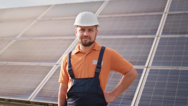 Porträtt av självsäker ingenjör av solcellsindustrin. Personal säker pose Solcellspanelinstallation. Närbild porträtt av manlig arbetare i skyddshjälm stående nära solpanel — Stockvideo