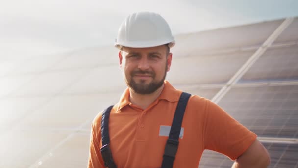 Ritratto ravvicinato di elettricista maschio in casco protettivo in piedi vicino al pannello solare. Produzione di energia pulita. Energia verde. Fattoria solare. Uomo allegro sorridente mentre in piedi alla fattoria di energia solare — Video Stock