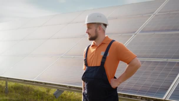 Güneş panelleri kurulumunun yanında duran üniformalı ekolojik uzman endüstriyel işçinin portresi. Güneş istasyonu inşaatı. İşçi. Temiz enerji üretimi. Yeşil enerji. Ekolojik güneş çiftliği. — Stok video