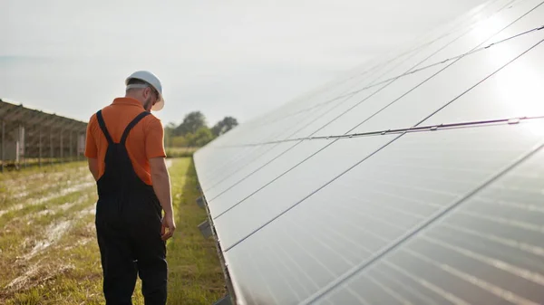 Ammattimainen miespuolinen insinööri suojakypärässä kävelee ekologisen aurinkovoimalan rakentamisessa. Käsite sähkö, ekologia, teknologiat. Aurinkopaneelien tila. Puhtaan energian tuotanto. Vihreä energia — kuvapankkivalokuva